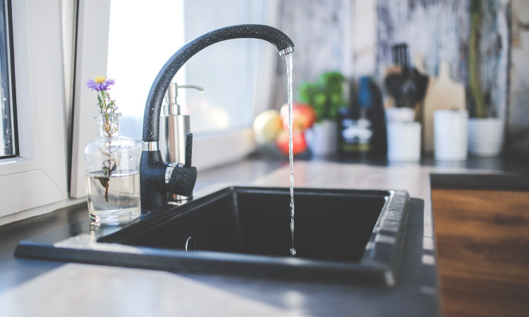 A stream of fluoridated water streams from a kitchen faucet next to a bright window