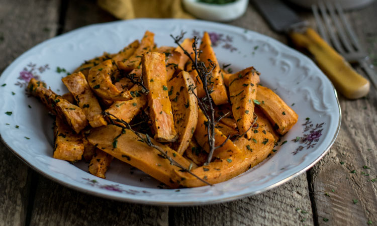 Closeup of a bowl of baked sweet potatoes slices topped with herbs for Thanksgiving