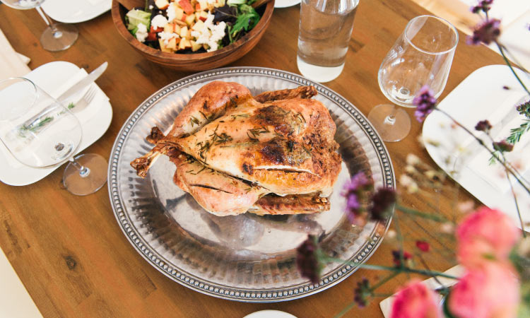 Aerial view of a Thanksgiving turkey on a silver platter next to water glasses, a salad, and a bouquet of flowers