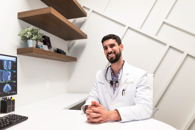 Dr. Perlman wears a white coat and smiles at their office, where he offers mercury-free dentistry