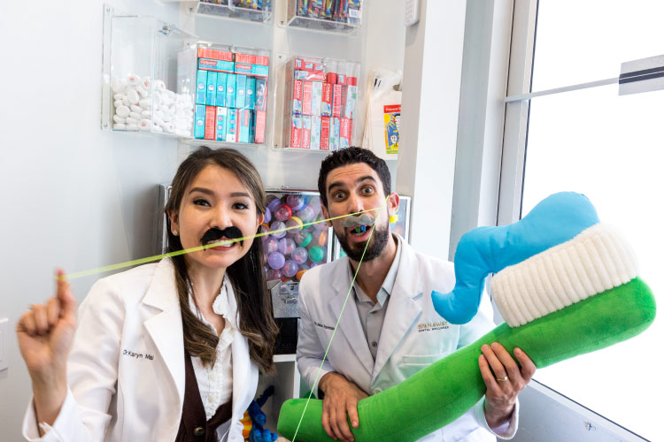 Dr. Perlman and Dr. Mai hold a large toothbrush while wearing fake mustaches