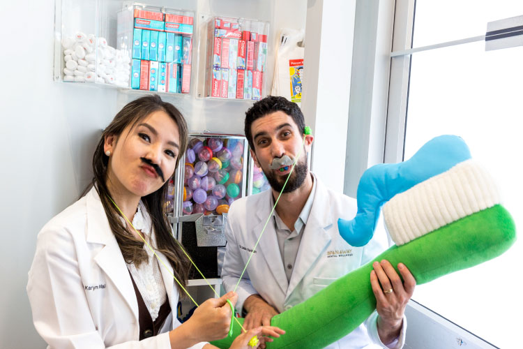 Dr. Mai and Dr. Perlman are wearing false mustaches and hamming it up with a big inflatable toothbrush to encourage good dental hygiene with your Invisalign, ClearCorrect or Six Month Smiles braces