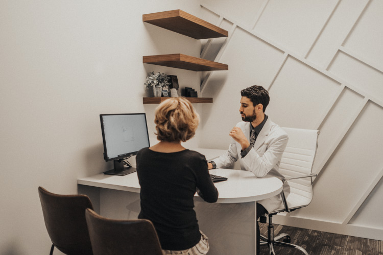 Woman sitting in a chair next to Dr. Perlman's desk consulting with him about a dental implant