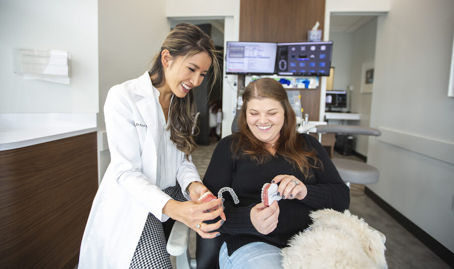 Dr. Mai shows a female patient her Invisalign aligners while she sits in the dental chair smiling